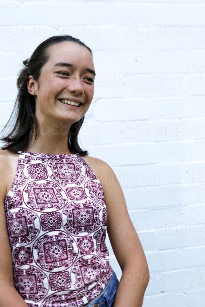 Portrait of young girl smiling in front of white brick wall - Australian Stock Image