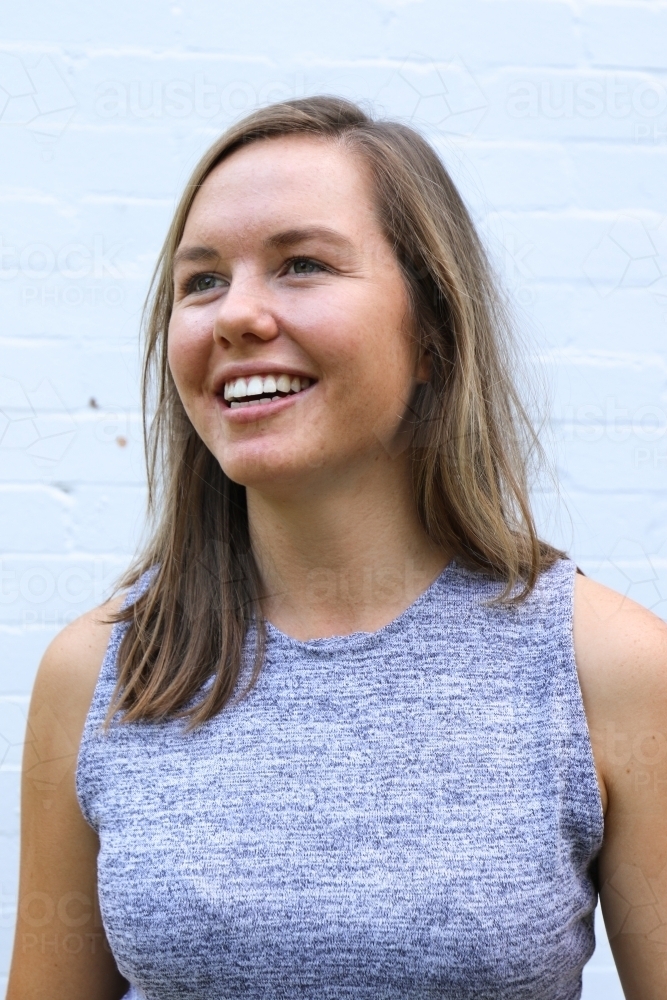 Portrait of young girl smiling in front of white brick wall - Australian Stock Image