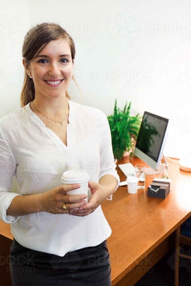Portrait of young professional woman holding a coffee in the office - Australian Stock Image