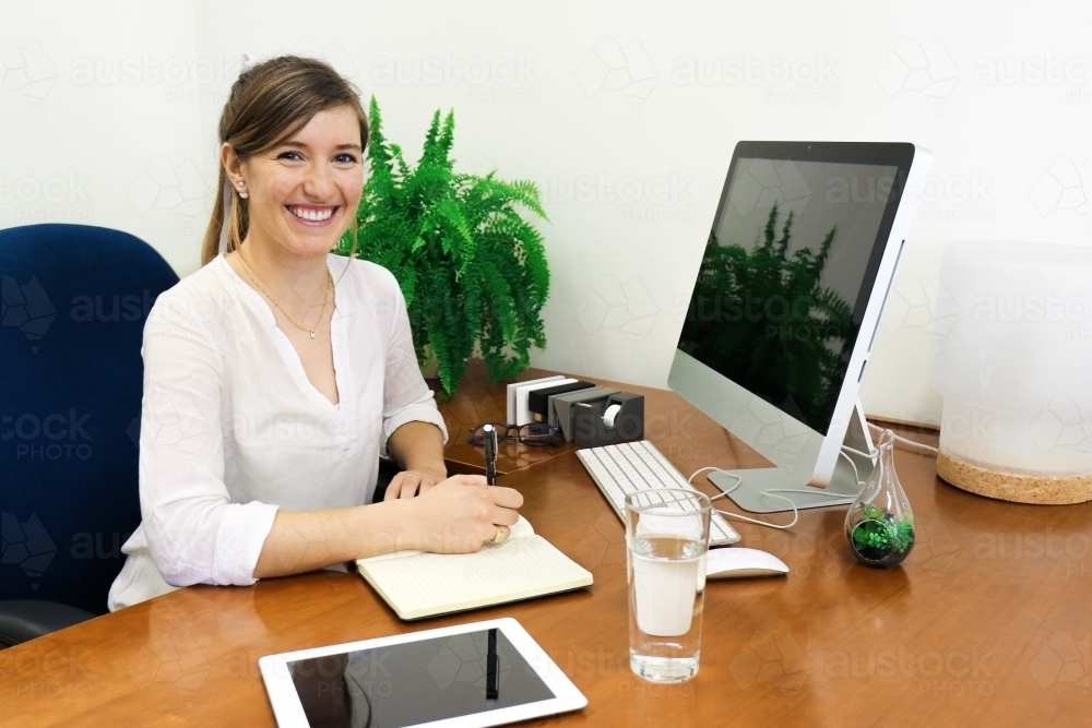 Portrait of young professional woman looking at camera from her office desk - Australian Stock Image