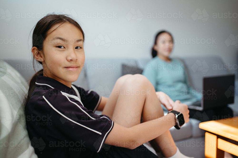 Pre-teen age girl sitting on the couch with mum on the other side - Australian Stock Image