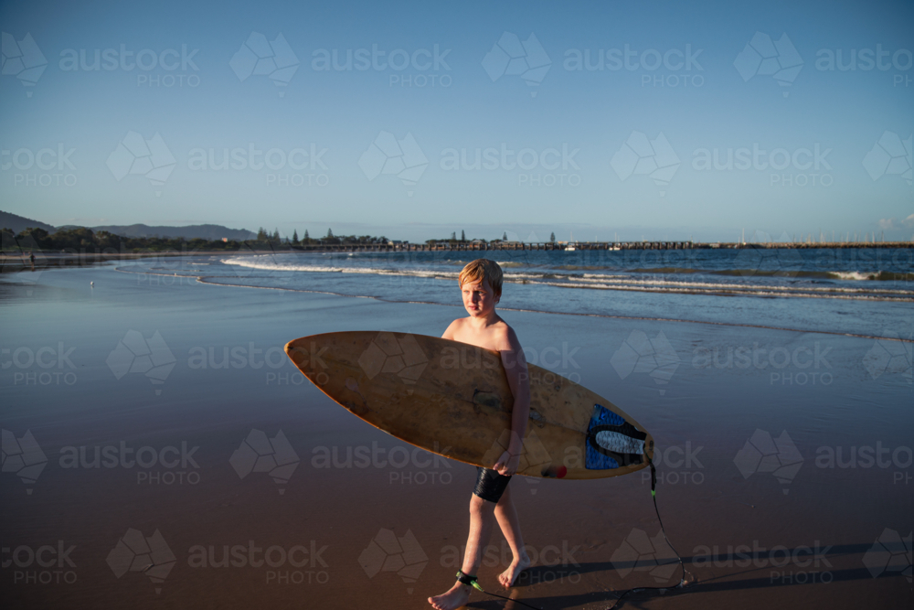 Pre-teen boy carrying surf board out of the water on the beach at Coffs Harbour - Australian Stock Image