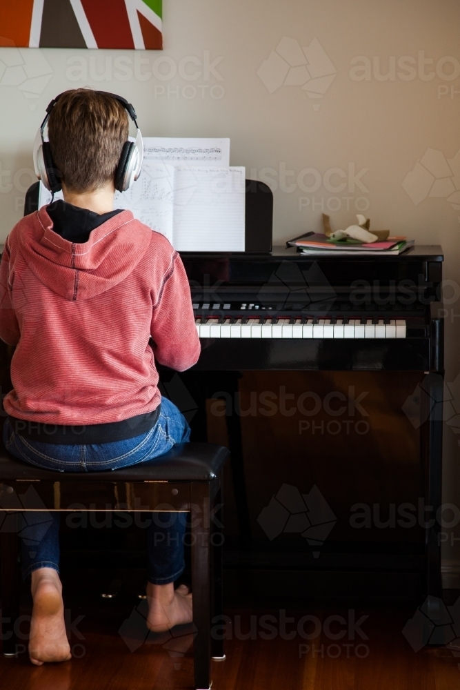 Pre-teen boy playing the piano with headphones on - Australian Stock Image