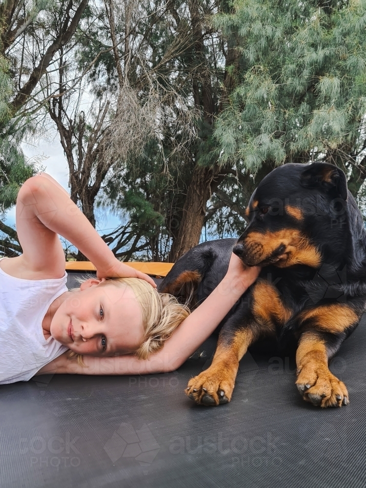 Pre-teen boy relaxing on trampoline with rottweiler dog - Australian Stock Image