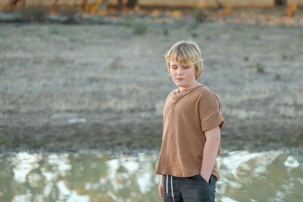 Pre-teen boy standing near creek in dry remote bush setting - Australian Stock Image