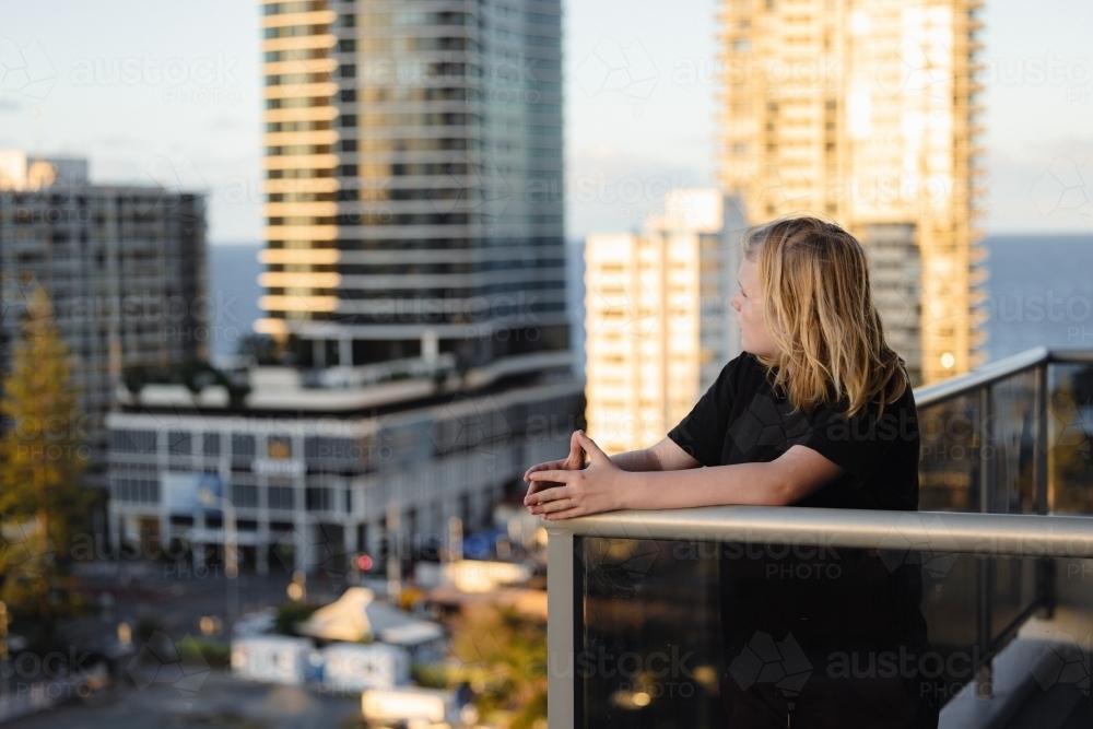 Pre-teen boy standing on balcony of high rise building on the Gold Coast with view of city - Australian Stock Image