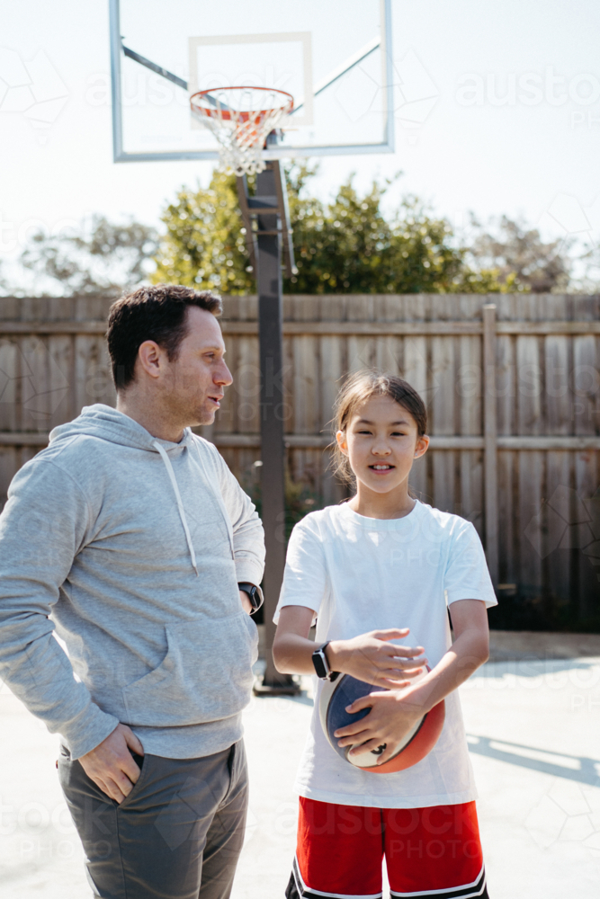 Pre-teen girl holding a ball beside his dad while standing in their yard - Australian Stock Image