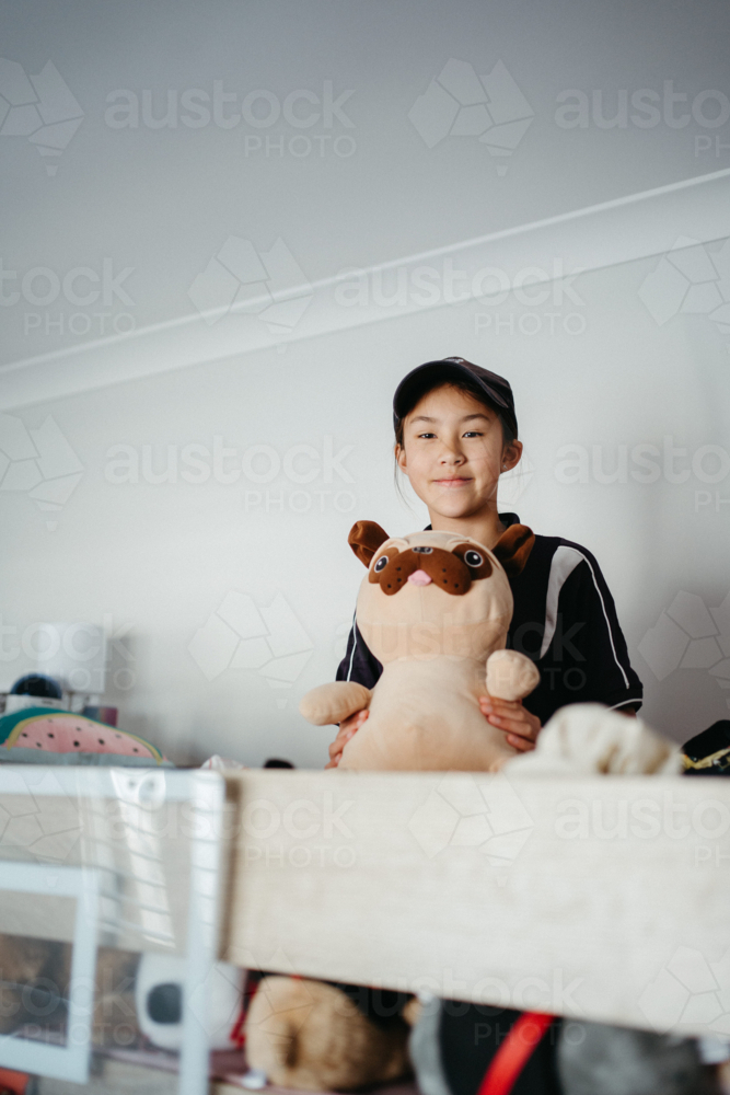 Pre-teen girl sitting on top of the bunk bed holding a plush toy. - Australian Stock Image