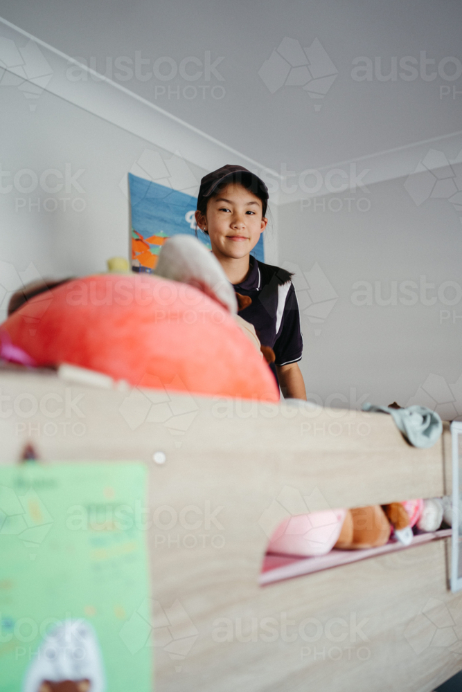 Pre-teen girl sitting on top of the bunk bed holding a plush toy - Australian Stock Image