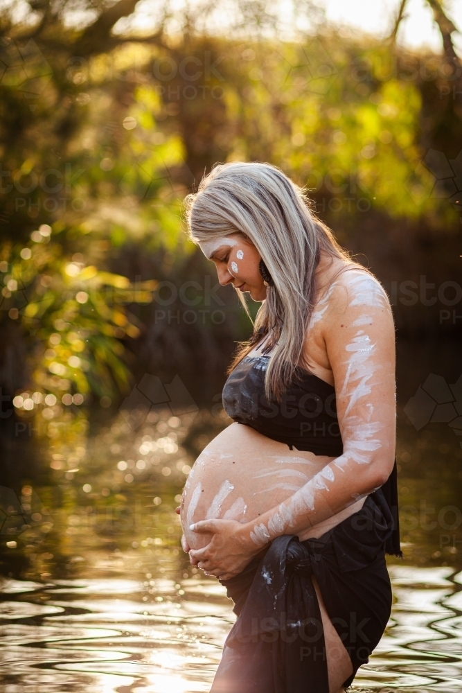 Pregnant Aboriginal Australian woman in sparkling billabong water on summer afternoon - Australian Stock Image