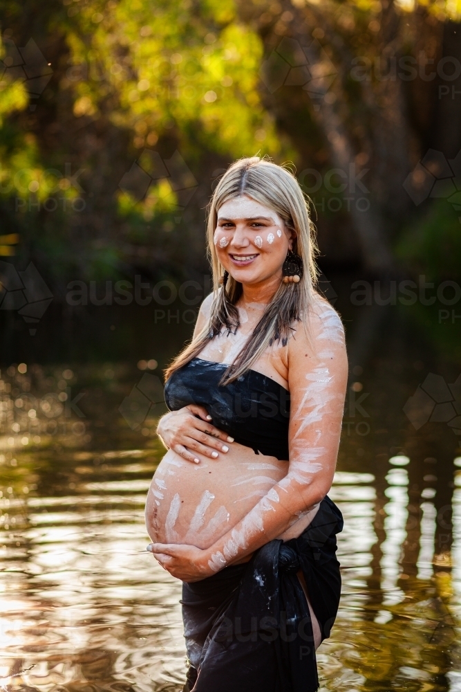 Pregnant Aboriginal Australian woman in sparkling billabong water on summer afternoon - Australian Stock Image