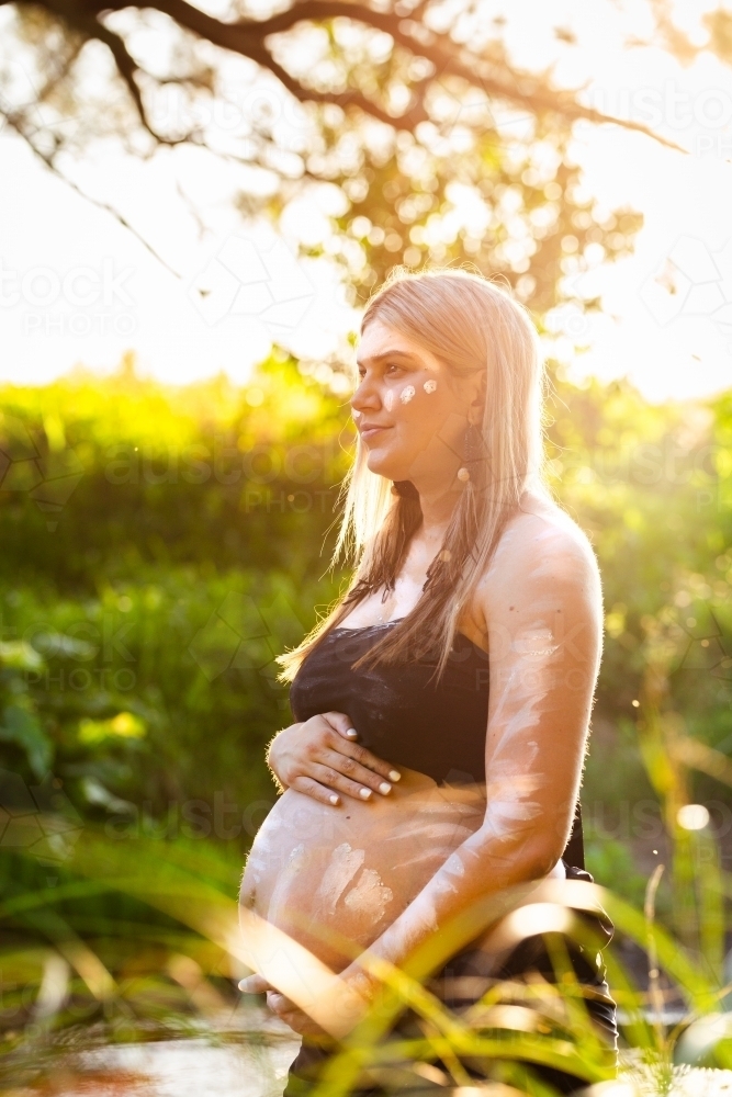 Pregnant Aboriginal Australian woman on country in traditional dreamtime ochre body paint - Australian Stock Image