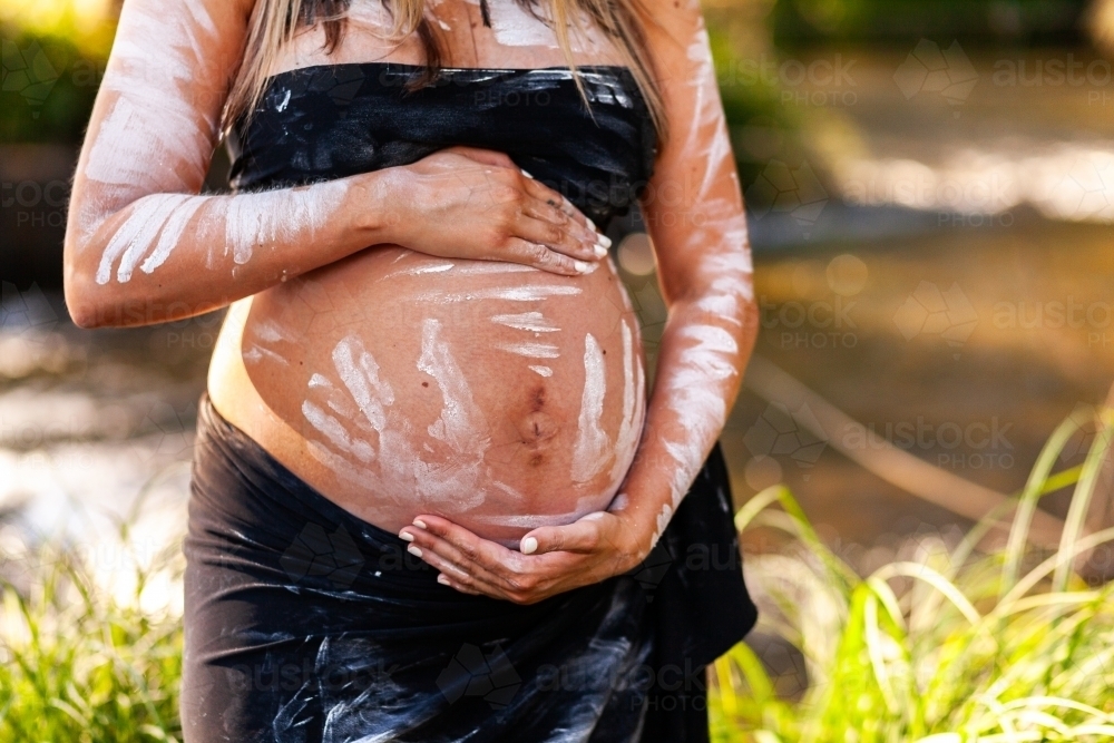 Pregnant Aboriginal lady in ochre body paint on country close up of belly - Australian Stock Image