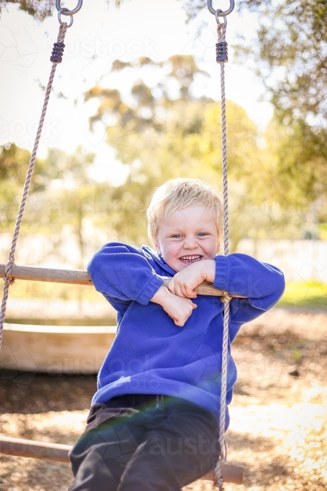 Preschool age child posing on rope ladder swing for kindergarten photos. Portrait of young boy. - Australian Stock Image