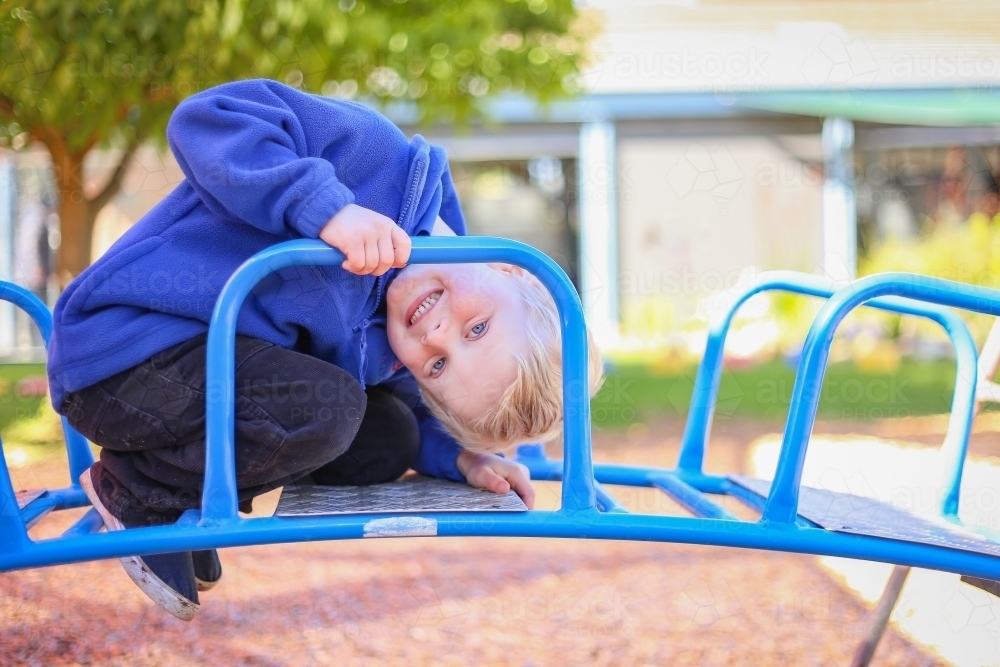 Preschool boy posing on climbing frame for kindergarten photos. Outdoor portrait of young boy - Australian Stock Image