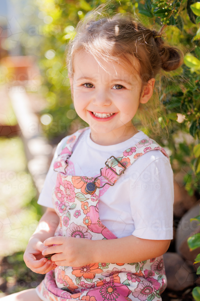 Preschool child sitting on edge of garden bed in bright sunny kindergarten yard - Australian Stock Image