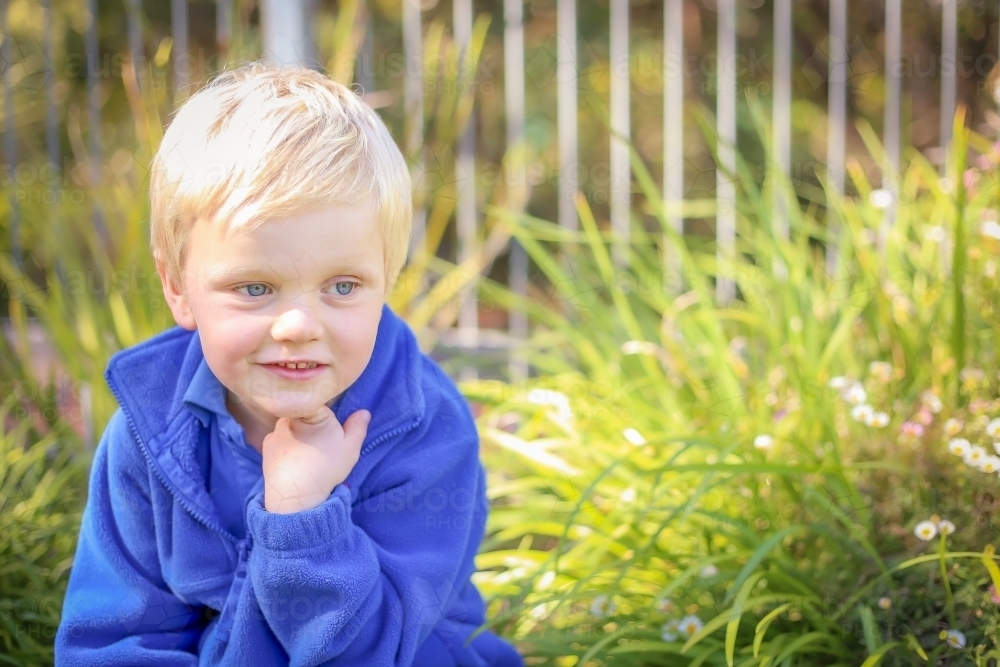 Preschooler sitting in garden with happy expression - Australian Stock Image