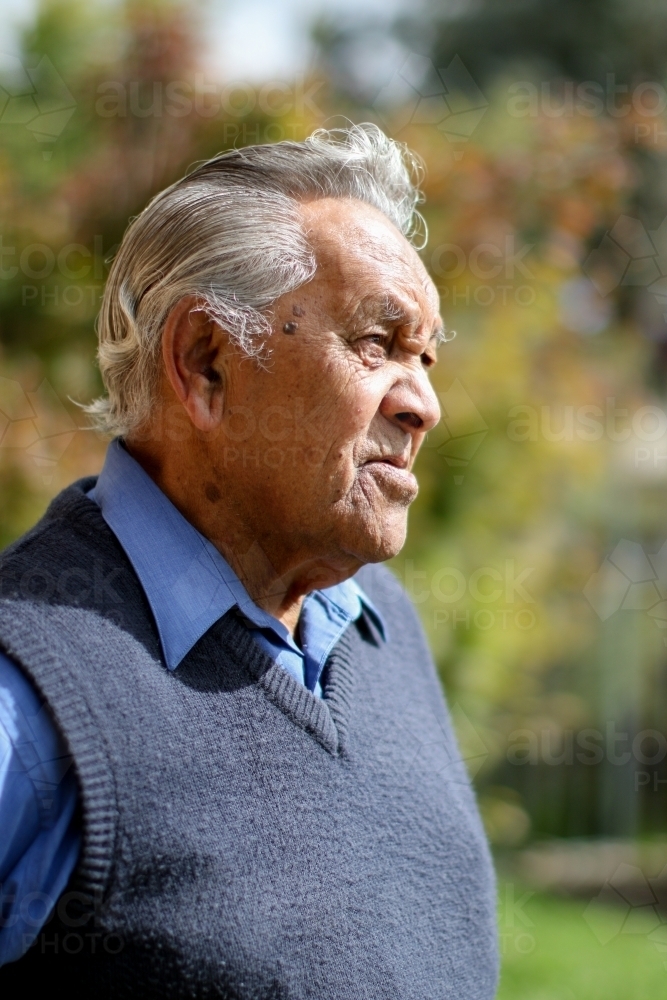 Profile of male Aboriginal elder in the sunlight with greenery in the background - Australian Stock Image