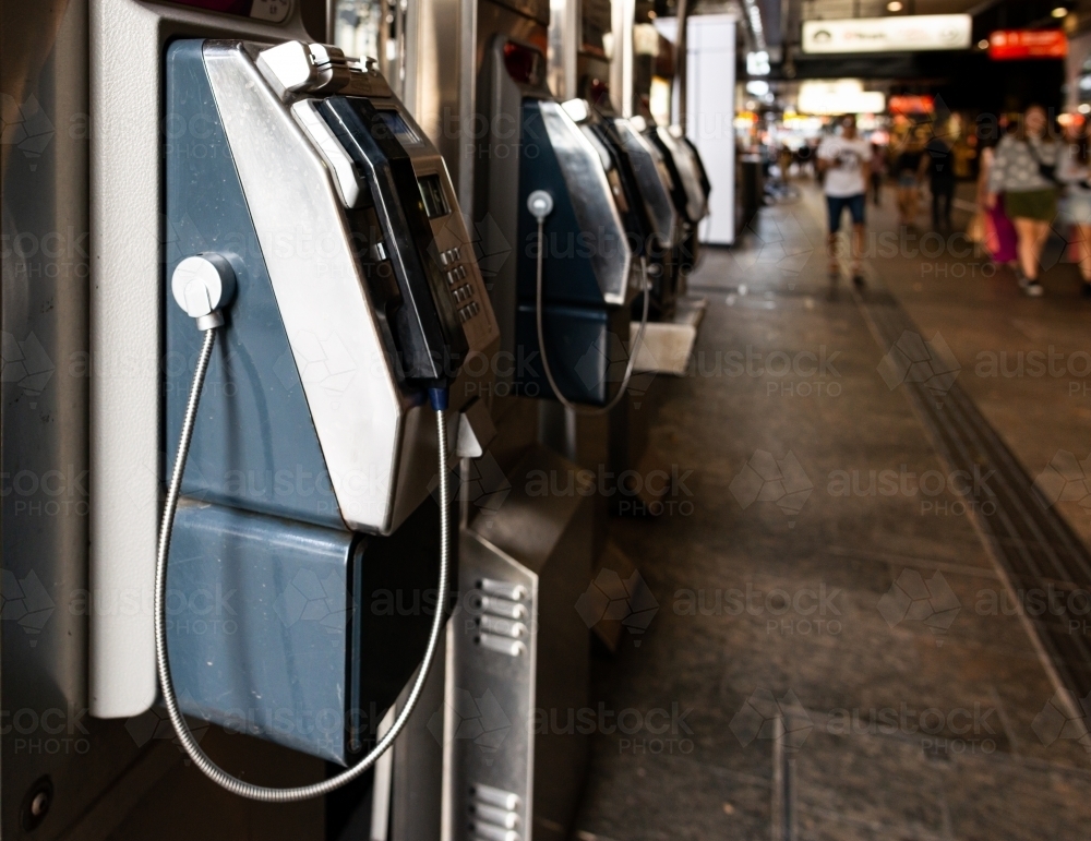 Public phones in city mall with people blurred in background - Australian Stock Image