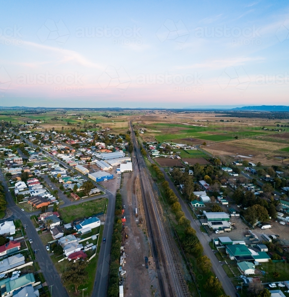 Railway tracks along edge of town with farm paddocks and dusk sky - Australian Stock Image