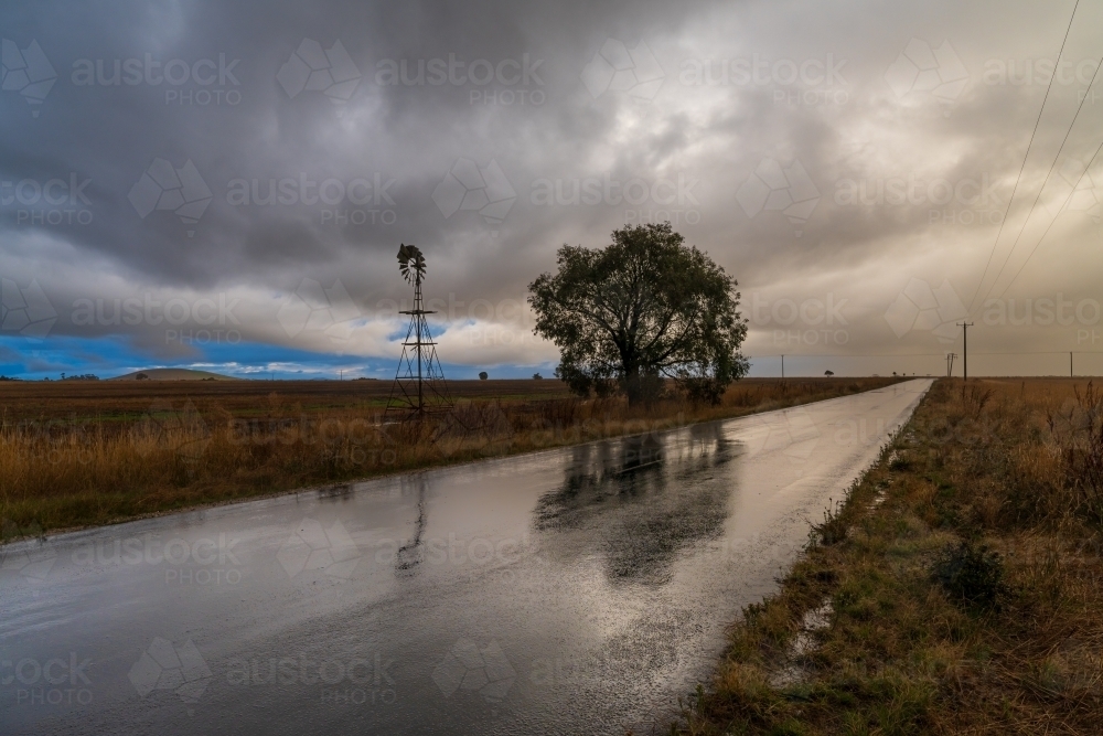 Rain falling from a dramatic stormfront over a long straight country road - Australian Stock Image