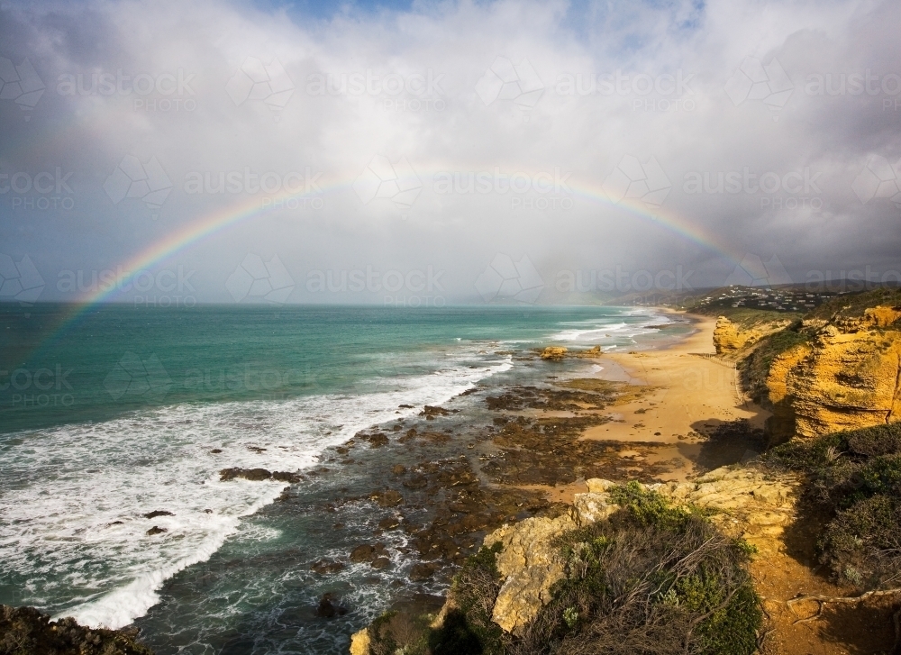 rainbow over coastal town and rugged coastline - Australian Stock Image