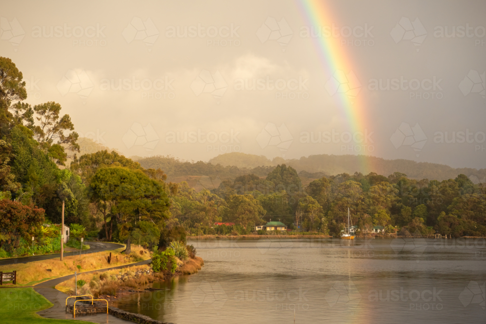 Rainbow over harbour waters with yacht on calm waters - Australian Stock Image