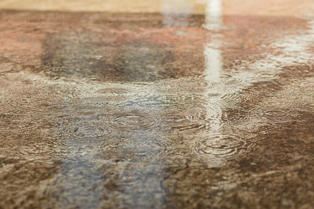 Raindrops splash in puddle on concrete driveway - Australian Stock Image