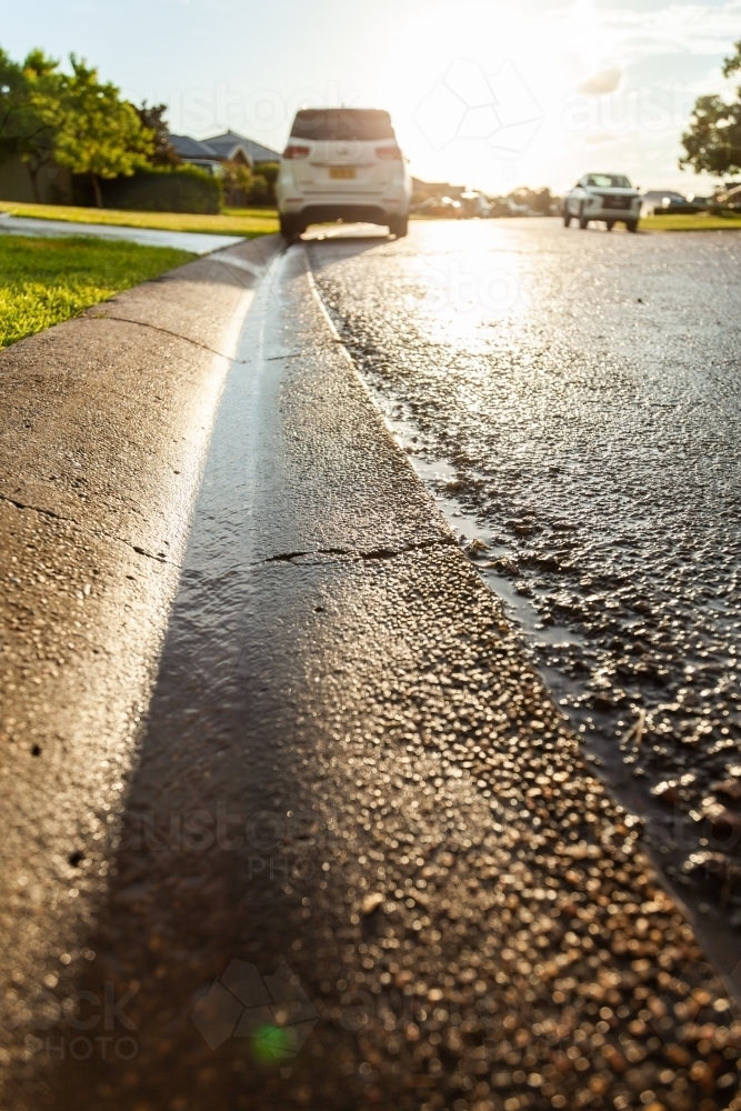 Rainwater running down gutter to stormwater drain in street - Australian Stock Image