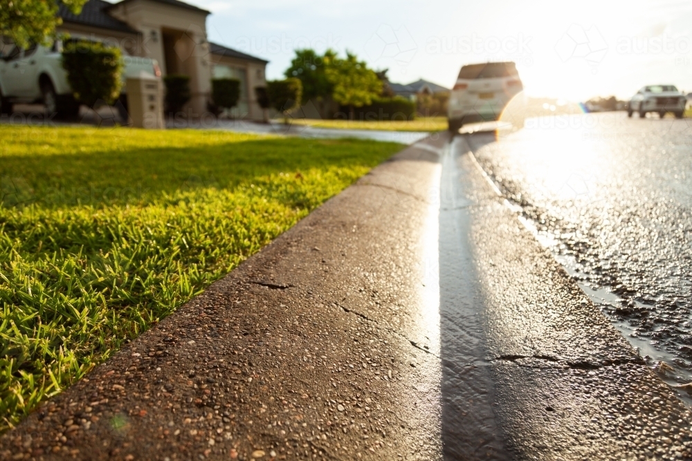 Rainwater running down gutter to stormwater drain in street - Australian Stock Image