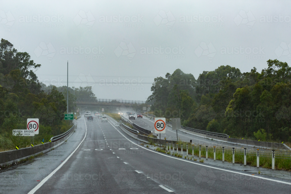 Rainy stormy day with cars driving on wet highway road with 80 speed zone signs - Australian Stock Image