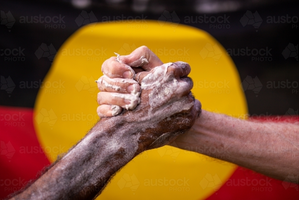 Reconciliation concept - indigenous hand clasped in front of aboriginal flag - Australian Stock Image