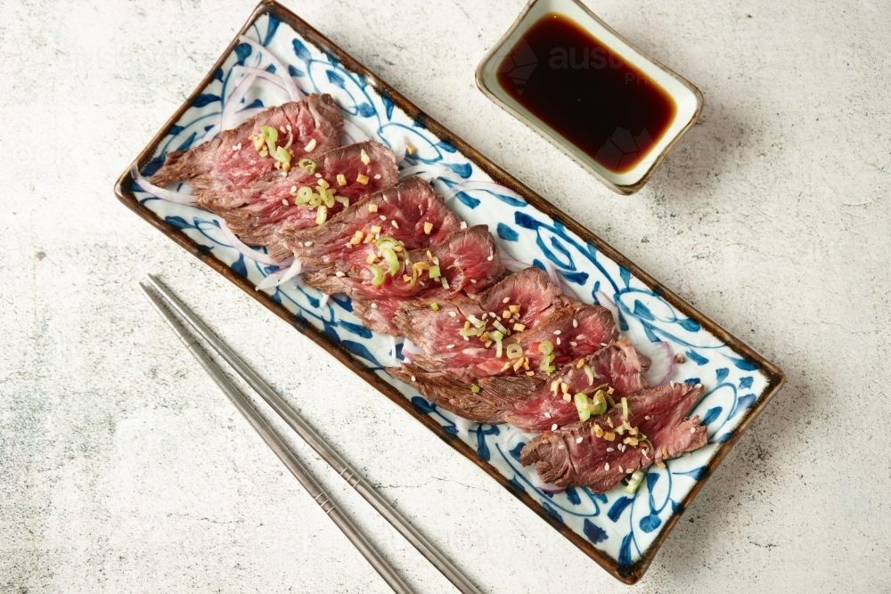 rectangular plate with thin slices of rarely cooked beef topped with green onions - Australian Stock Image