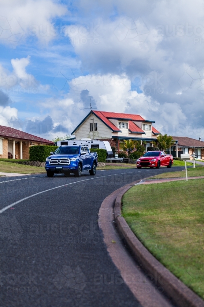 Red and blue car going round corner in road with house behind on hill - Australian Stock Image