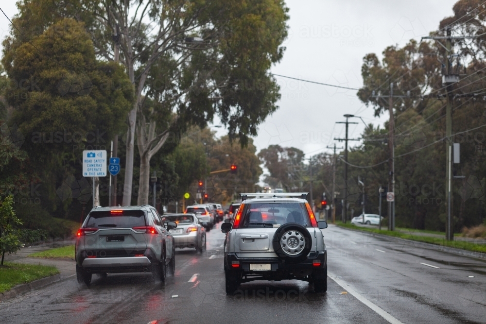 Red break lights of cars on slippery wet road stopping at traffic light - Australian Stock Image