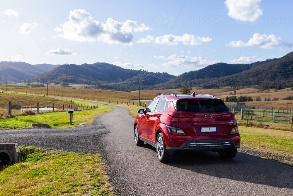 Red electric vehicle car driving down rural country road in hills of Stanhope, NSW, Australia - Australian Stock Image