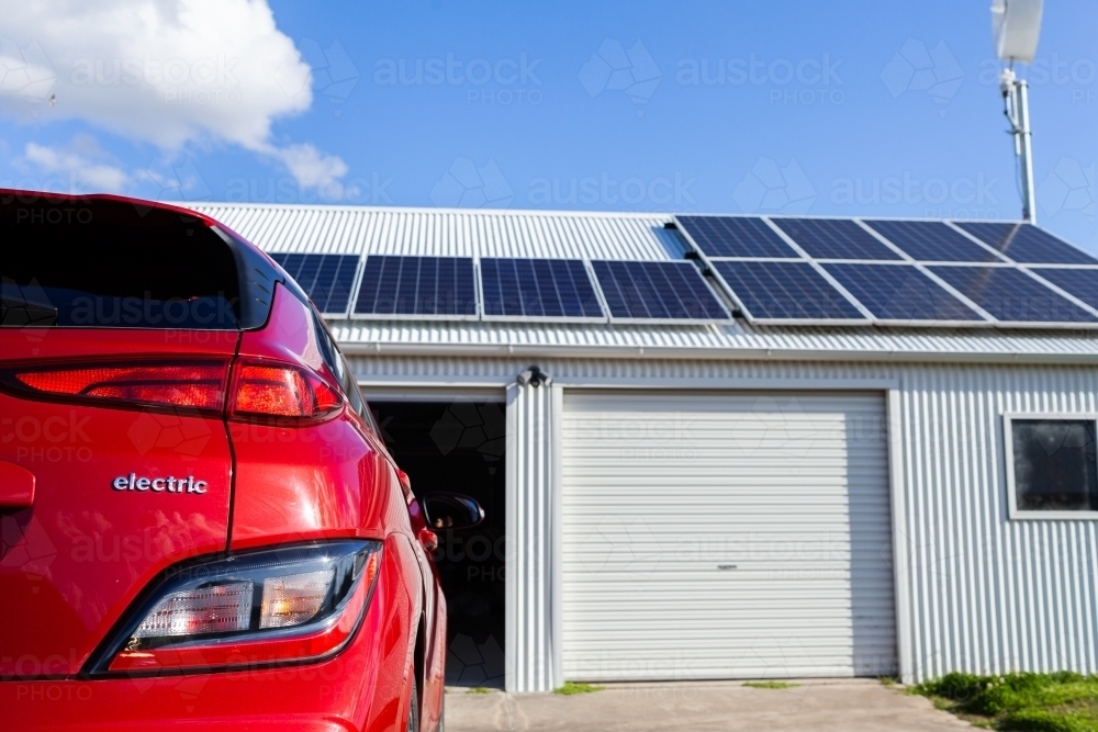 Red electric vehicle with copy space and out of focus solar panels on roof in background - Australian Stock Image