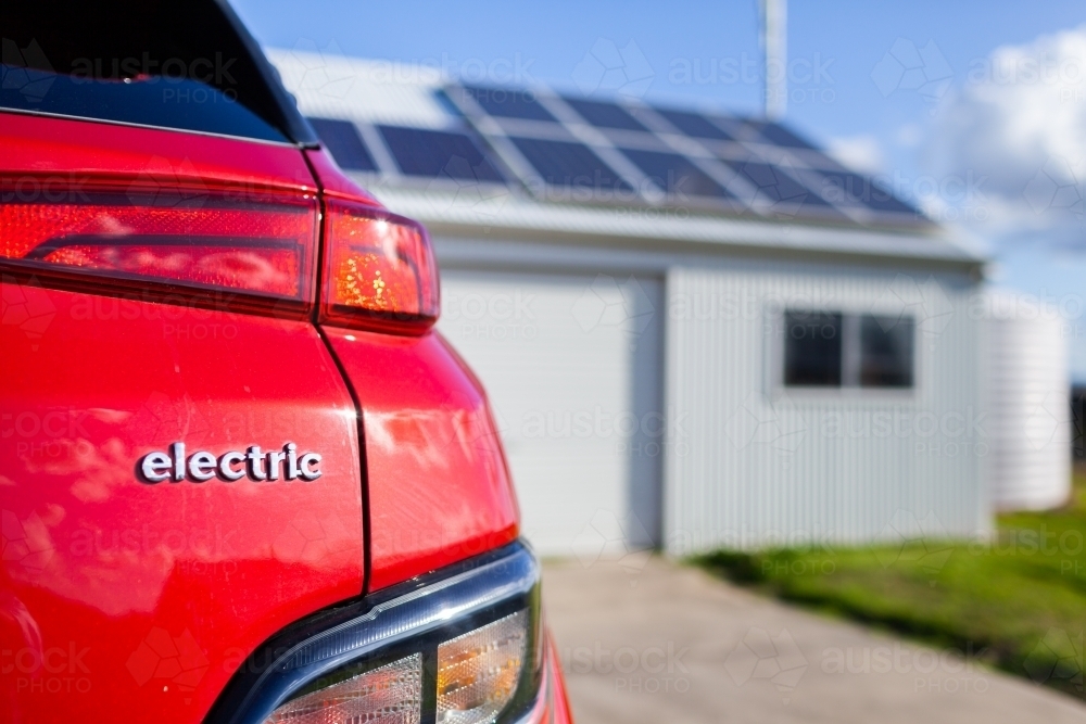 Red electric vehicle with copy space and out of focus solar panels on roof in background - Australian Stock Image