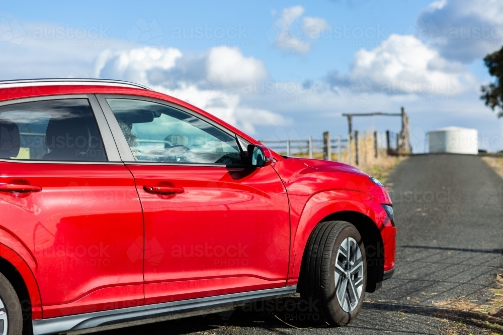 Red ev car driving into driveway of rural property - Australian Stock Image