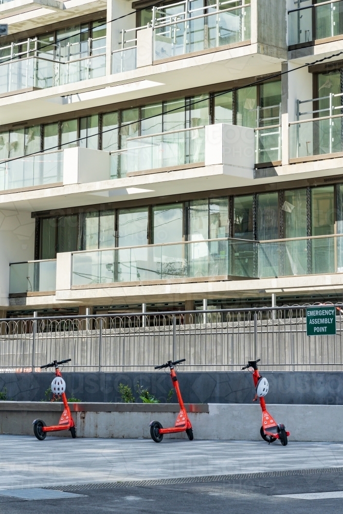 Red hire scooters parked in a courtyard at the base of an apartment building - Australian Stock Image