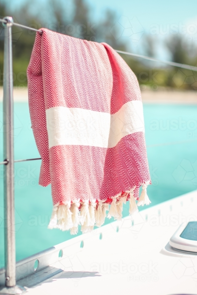 Red turkish towel hanging on wire railing of boat on the water - Australian Stock Image