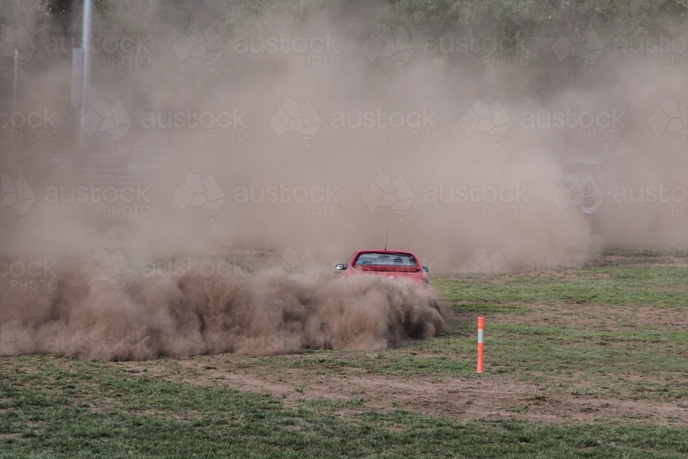 Red ute driving in show ground making dust clouds - Australian Stock Image