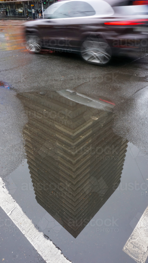 Reflection of a high rise building in a street puddle after rain - Australian Stock Image