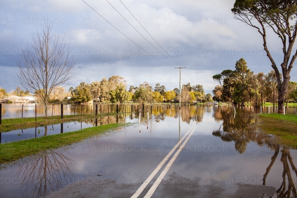 reflection of tree in flood water over road in town near golf course - Australian Stock Image