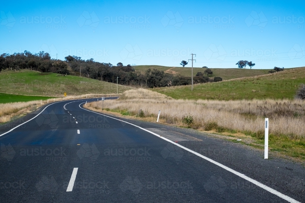 Regional road surrounded by hills and a clear blue sky - Australian Stock Image