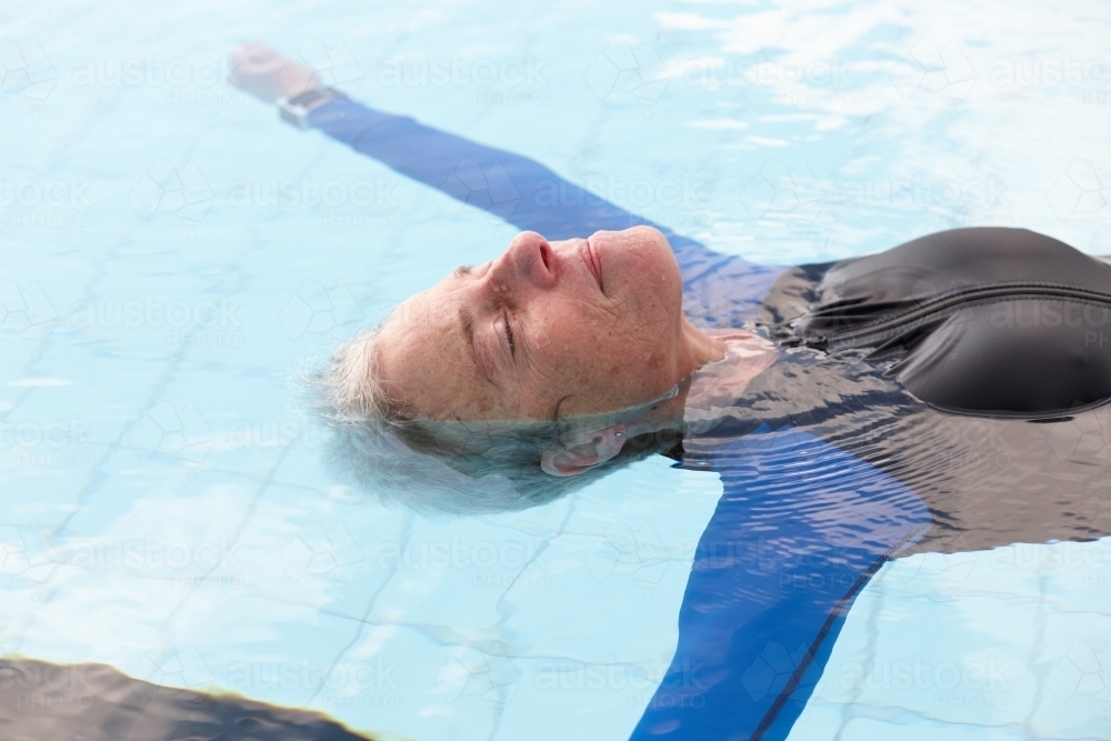 Relaxed active senior lady floating in swimming pool - Australian Stock Image