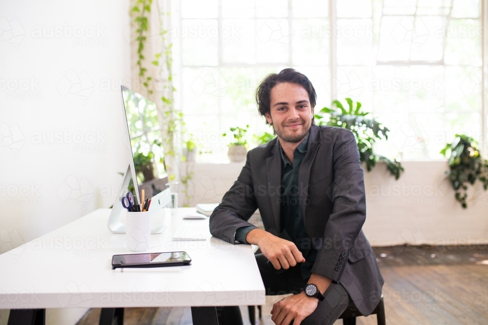 Relaxed businessman sitting and smiling in minimal creative office - Australian Stock Image