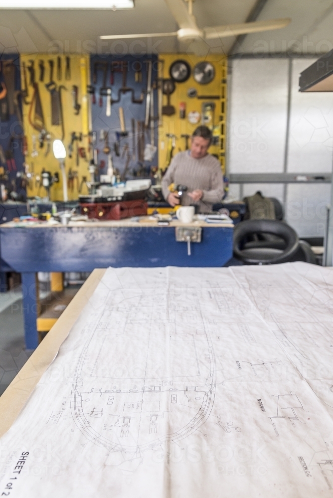 Retired Man Working On Hobby Boat Plan In Foreground - Australian Stock Image