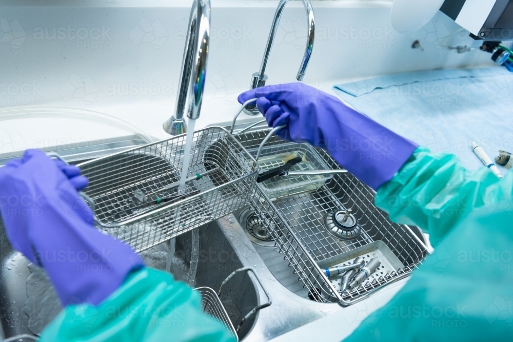 Rinsing and cleaning dental instruments under running water - Australian Stock Image