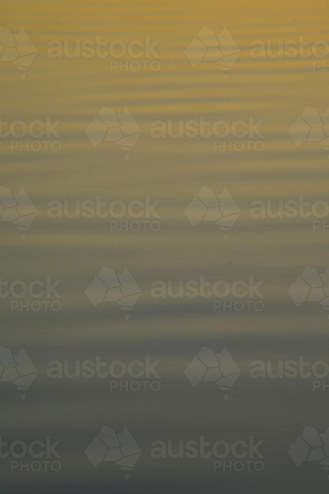 Ripples on a serene lake reflecting sunset colours - Australian Stock Image